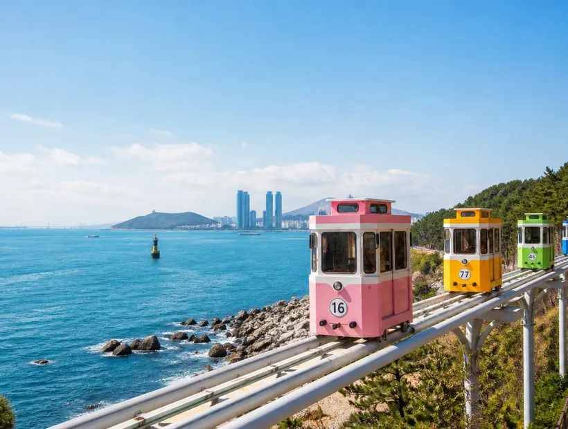 釜山海雲台藍線公園天空膠囊沿海行駛,粉彩車廂與碧海藍天,白天示意